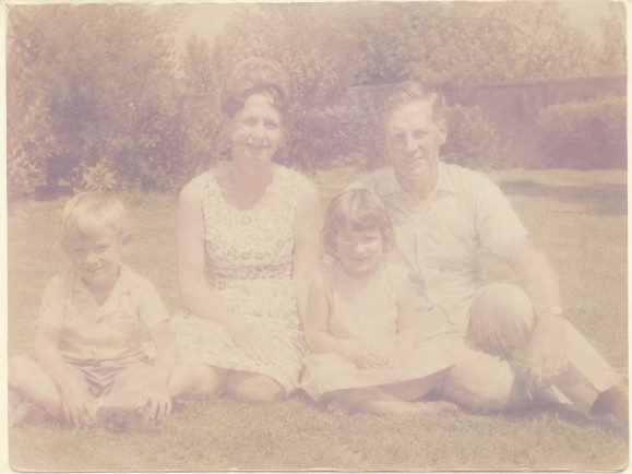 Heavily faded vintage family photograph with washed-out colours, reduced contrast and loss of detail caused by age and sun exposure.